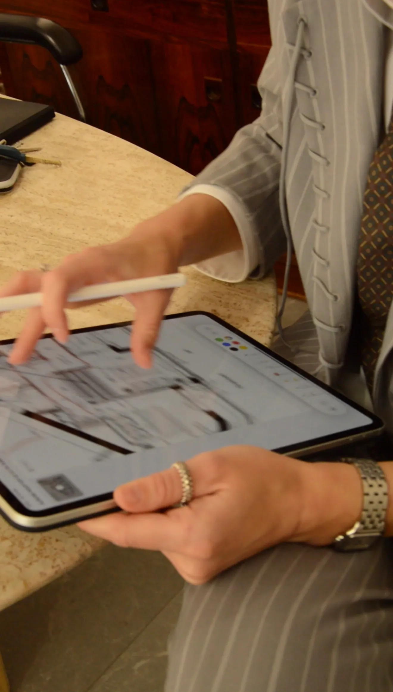 Person in pinstripe suit holding a tablet and using a stylus to draw architectural floor plans.