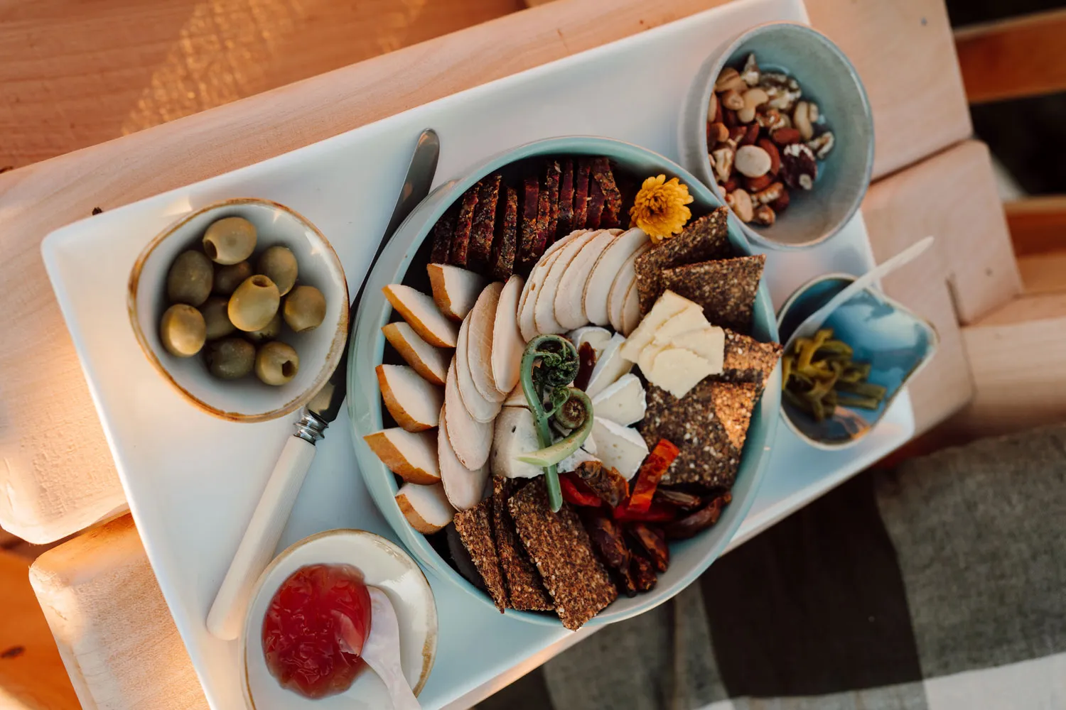 Charcuterie plate with assorted sliced meats, cheeses, crackers, nuts, olives, and condiments on a wooden table.