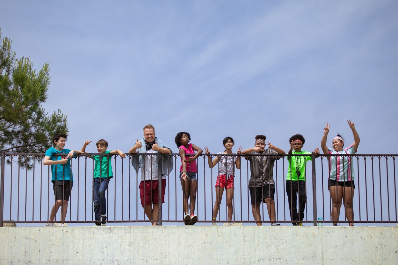 Photo of a camp counselor with a group of seven campers smiling and giving thumbs-ups and peace signs.