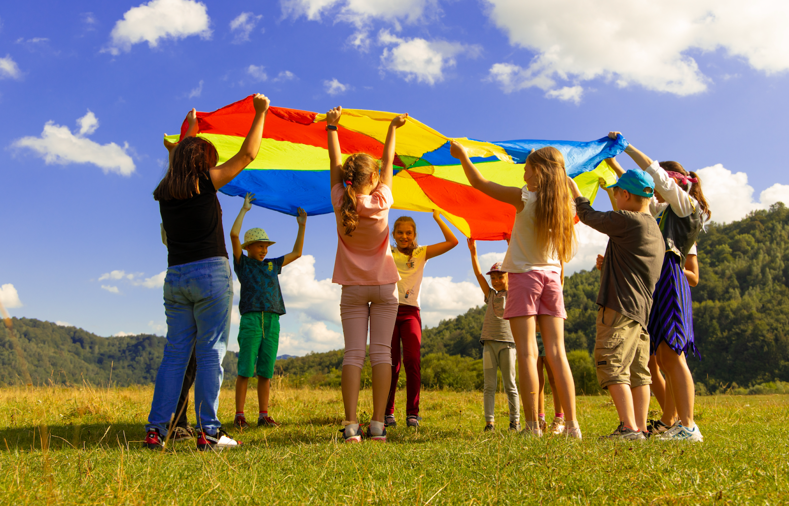 Young campers lift a yellow, blue, and red parachute above their heads during a game.