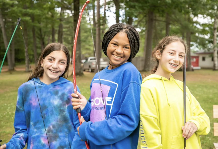 Three girls posing with bows on the archery field.