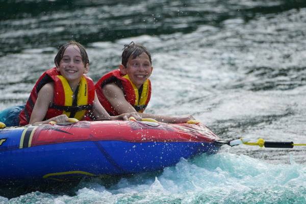 Summer camp participants on a lake being towed on an inflatable behind a boat