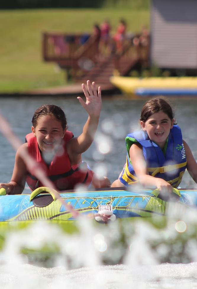 Two summer camp participants towed behind a boat on the lake at Camp Silver Lake
