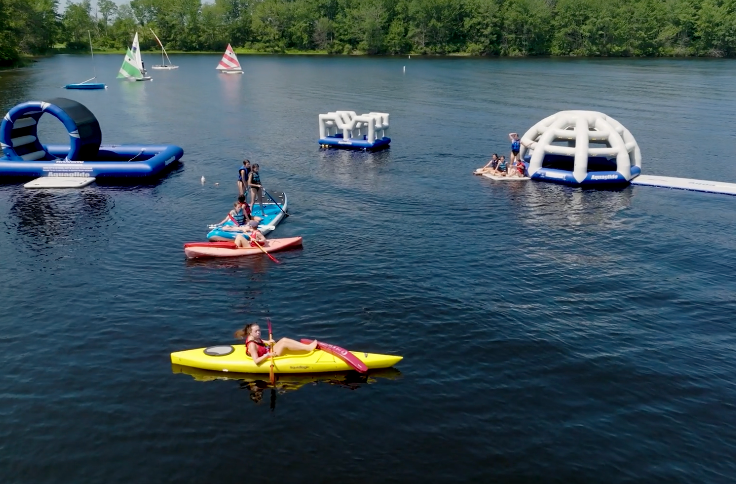 Camp counsellors and campers kayaking and sailing on a lake
