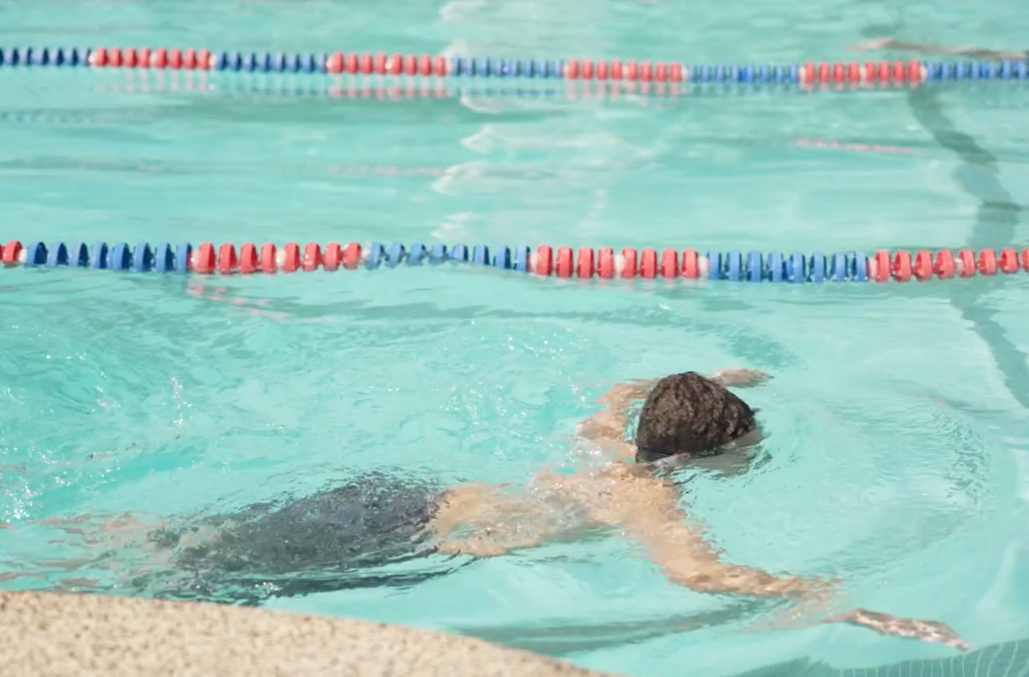 A summer camp participant swimming in a pool at camp