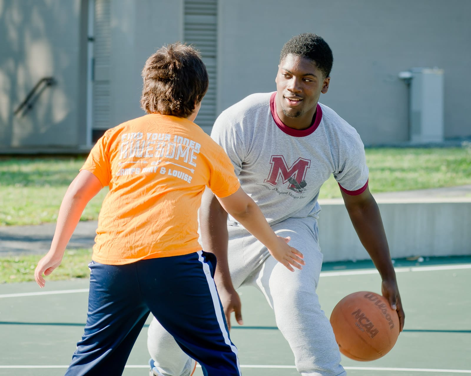 A camp counsellor and a camper at Camp Airy for Boys playing basketball on an outdoor court