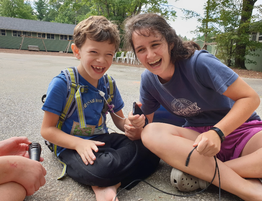  A counsellor and a child sitting outdoors laughing at Camp Allen