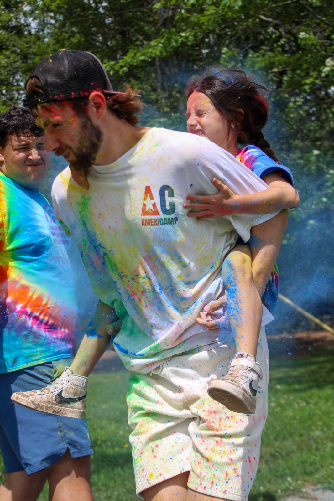 Camp counsellor piggybacking young camper, both covered in colorful paint