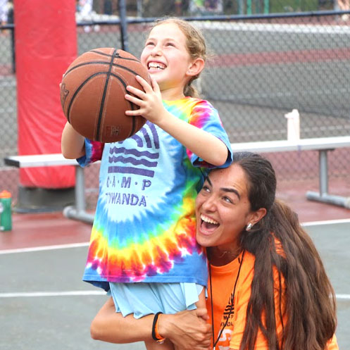 A Camp Towanda camp counsellor lifting up a young camper holding a basketball