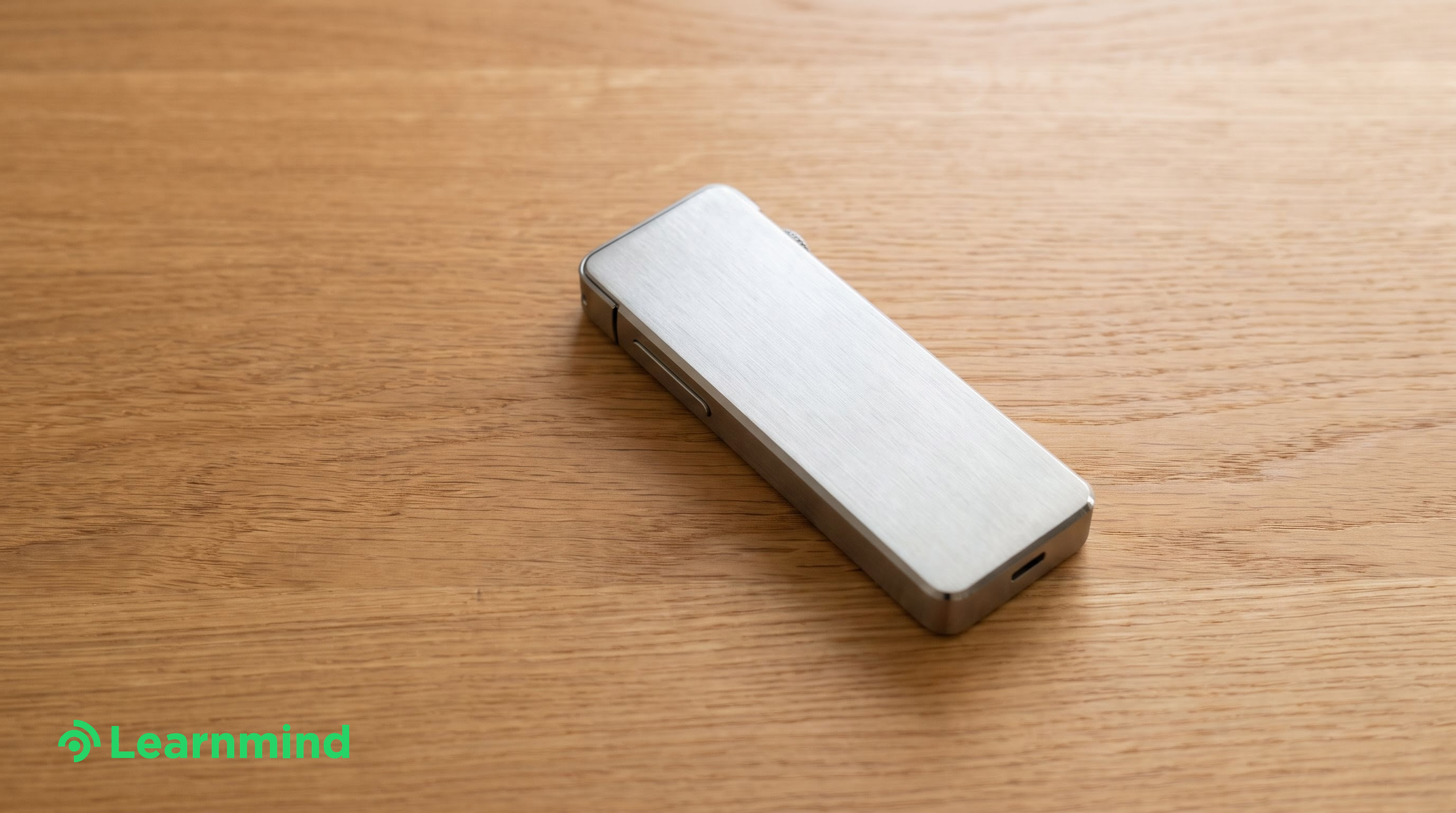 Brushed metal recorder device on warm wood desk, bright daylight