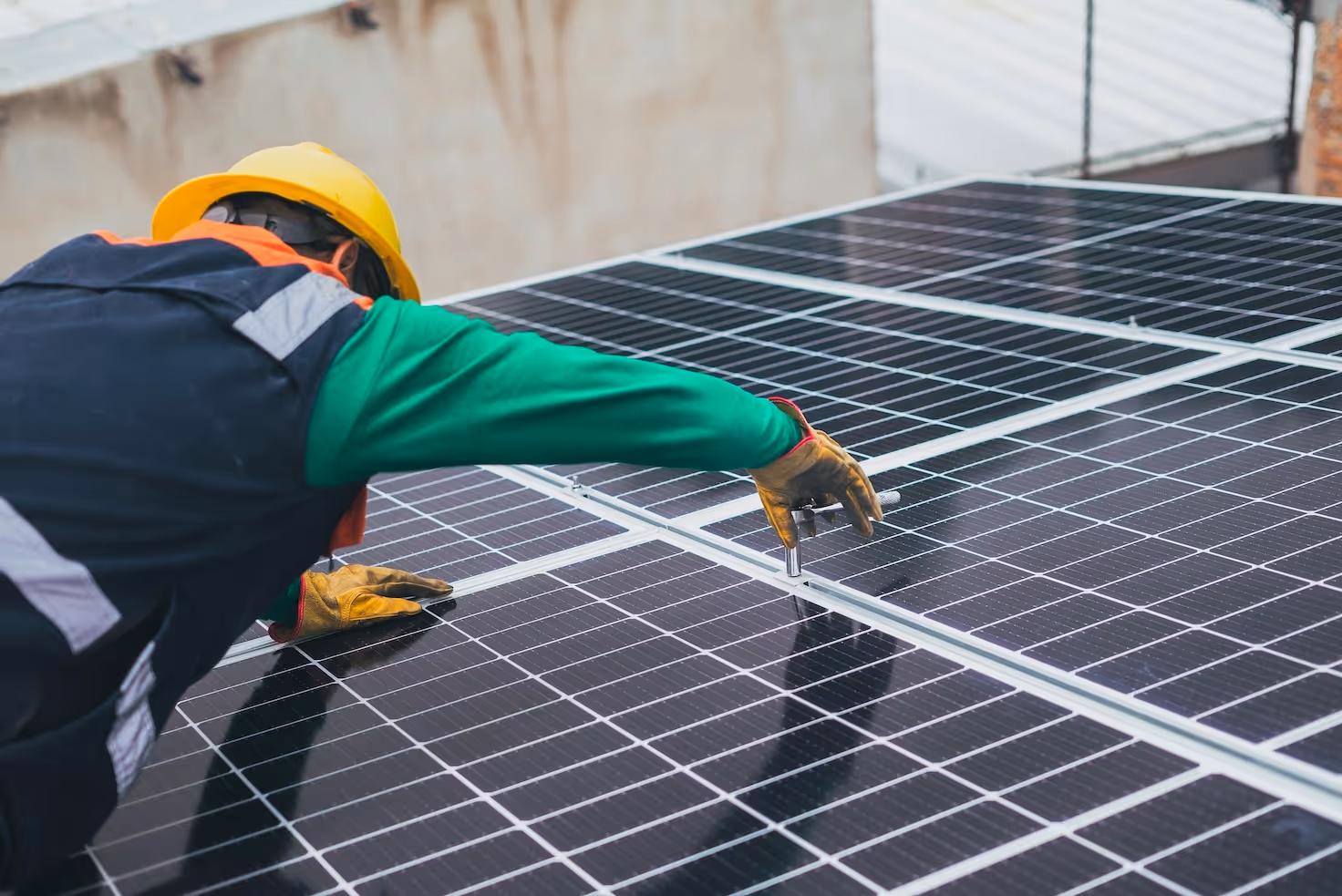 Arbeiter mit Schutzhelm und Handschuhen montiert eine Photovoltaikanlage auf einem Dach, sichtbar sind mehrere Solarpaneele.