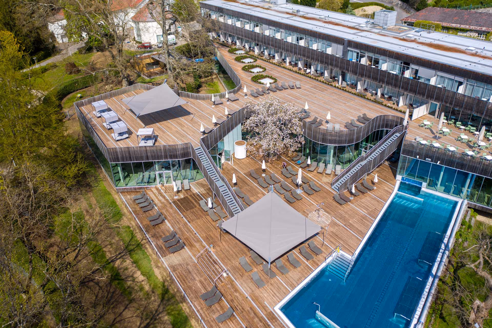 Kurhaus Bad Gastein — A spacious hotel terrace with a modern wooden deck and two free-standing SunSquare sun sails over the pool and lounge area. Elegant sun protection for spa guests.