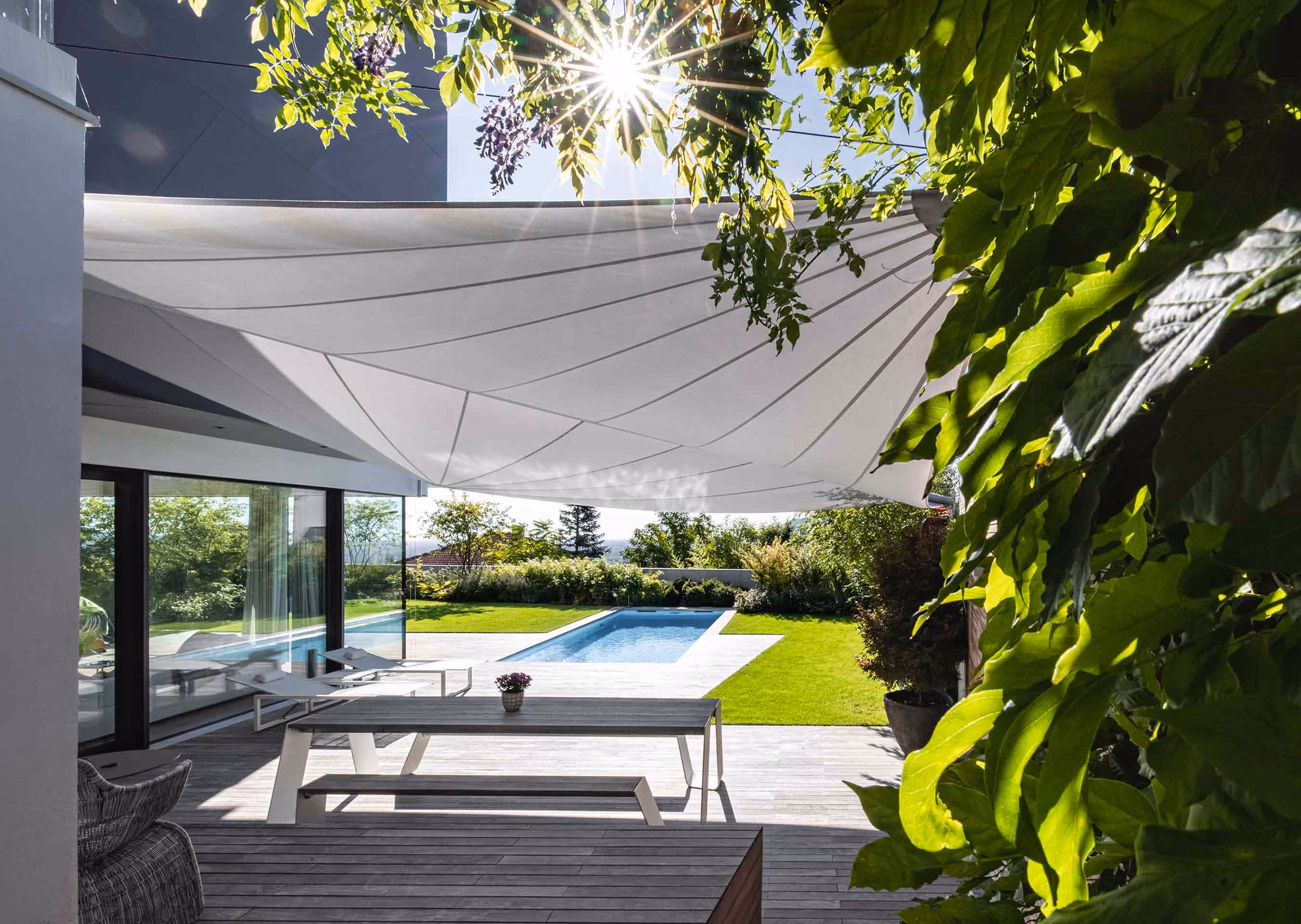 Modern sun sail over a stylish terrace with pool — elegant sun protection in a private garden.