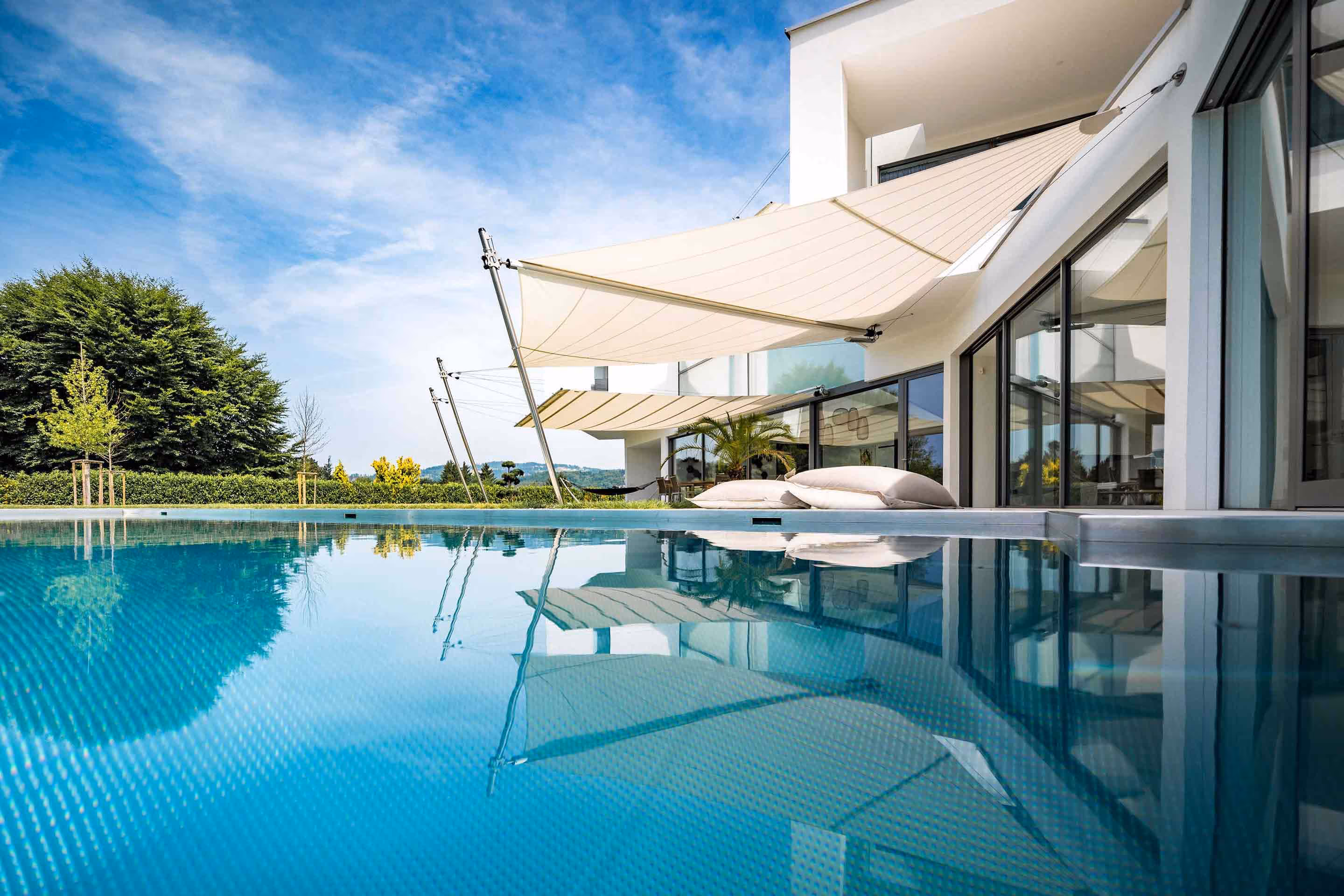 Two SunSquare shade sails provide shade for a pool and the adjacent outdoor lounge. The living area is extended to the outside, the boundaries between inside and outside are blurred.