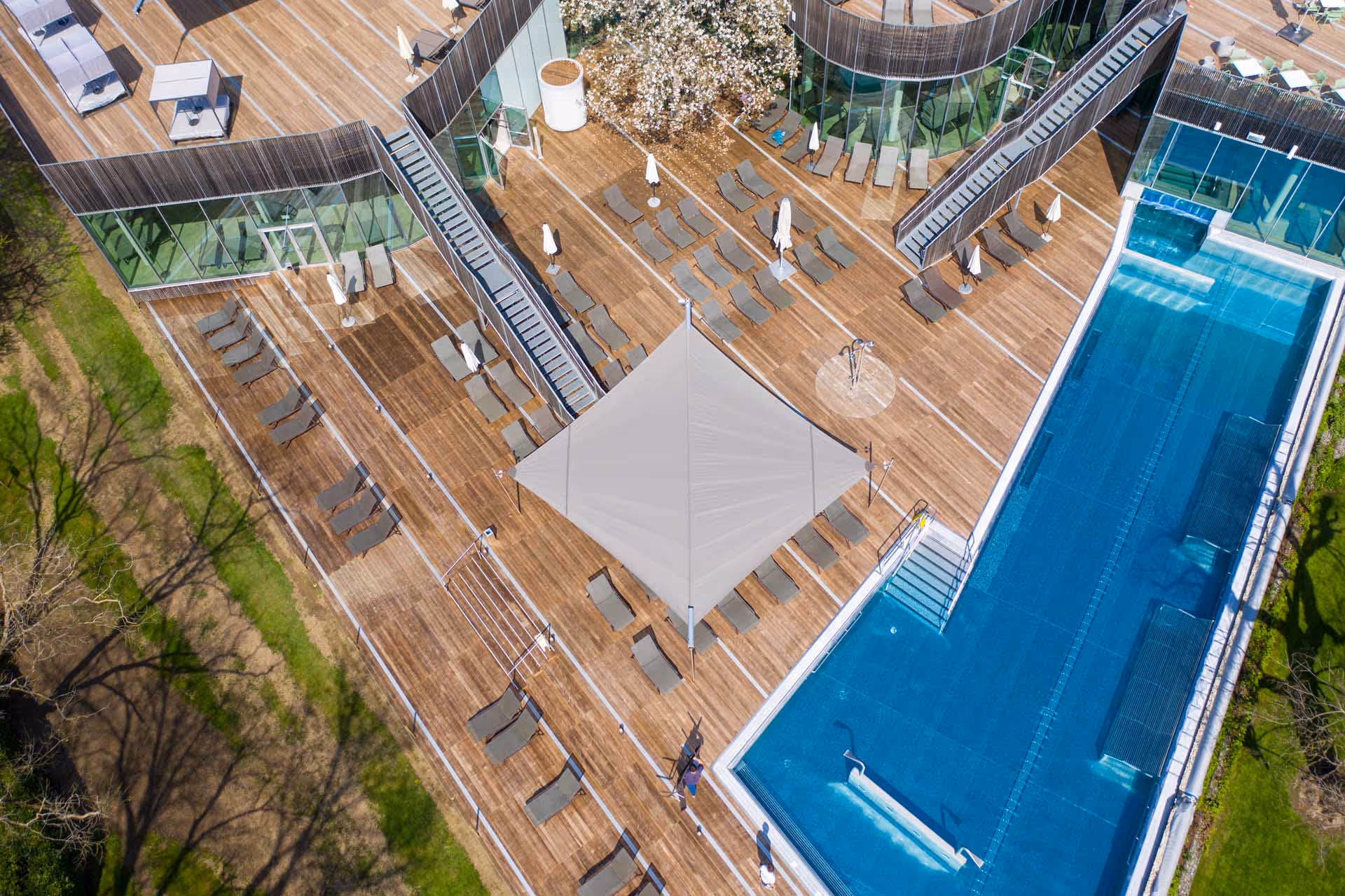 Luftaufnahme einer modernen Hotelterrasse mit großzügigem Holzdeck, zahlreichen Liegestühlen und SunSquare Sonnensegel. Ein großes, dreieckiges SunSquare-Sonnensegel spendet Schatten.