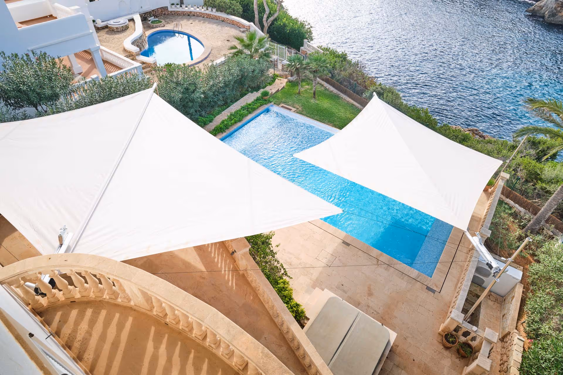 Two SunSquare shade sails built on different levels provide shade for a terrace and on the lower level for a swimming pool located near the sea.