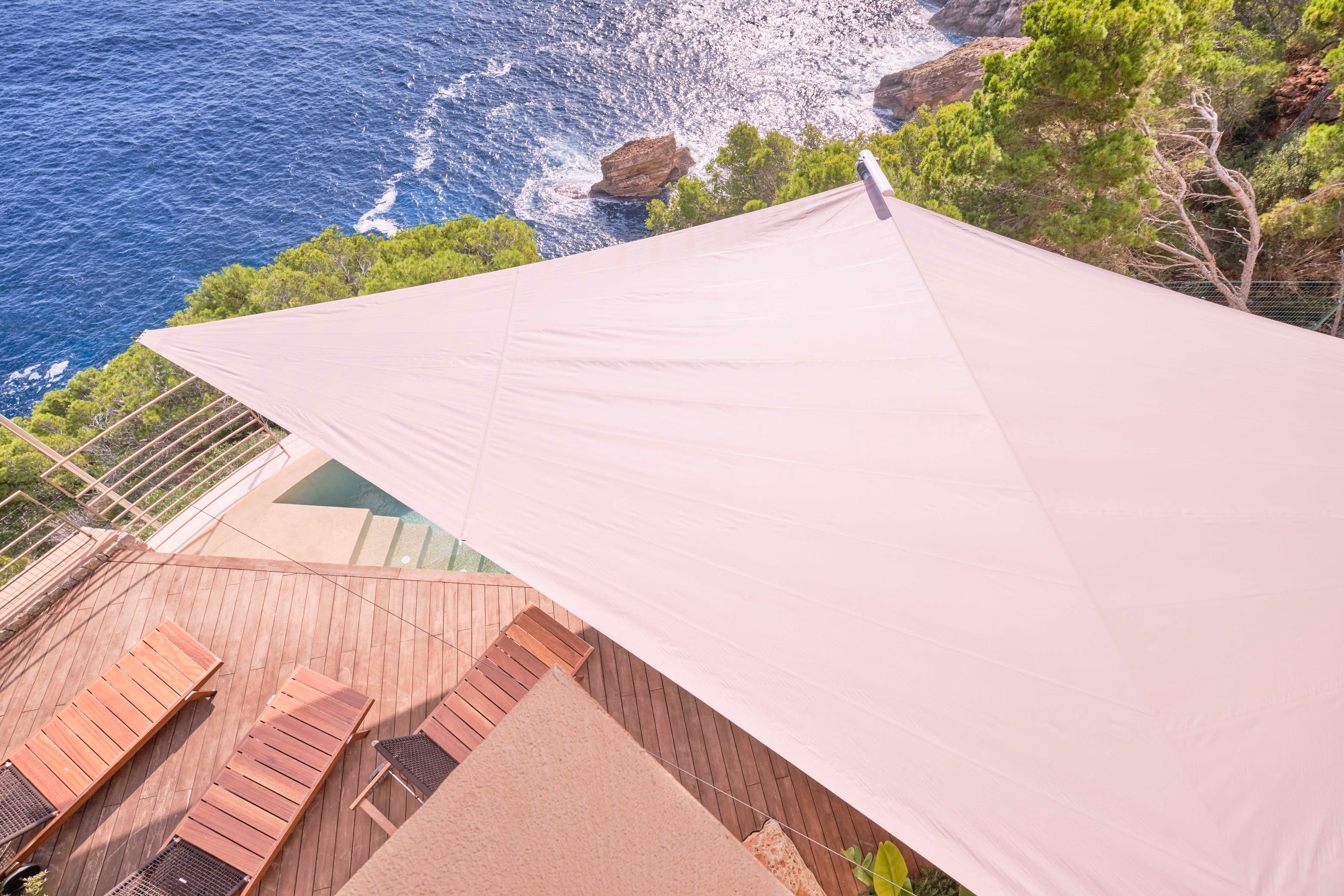 Ein Blick die Steilküste hinunter, man sieht ein Segel von oben und Meter darunter das Meer, das an die Felsen schlägt.