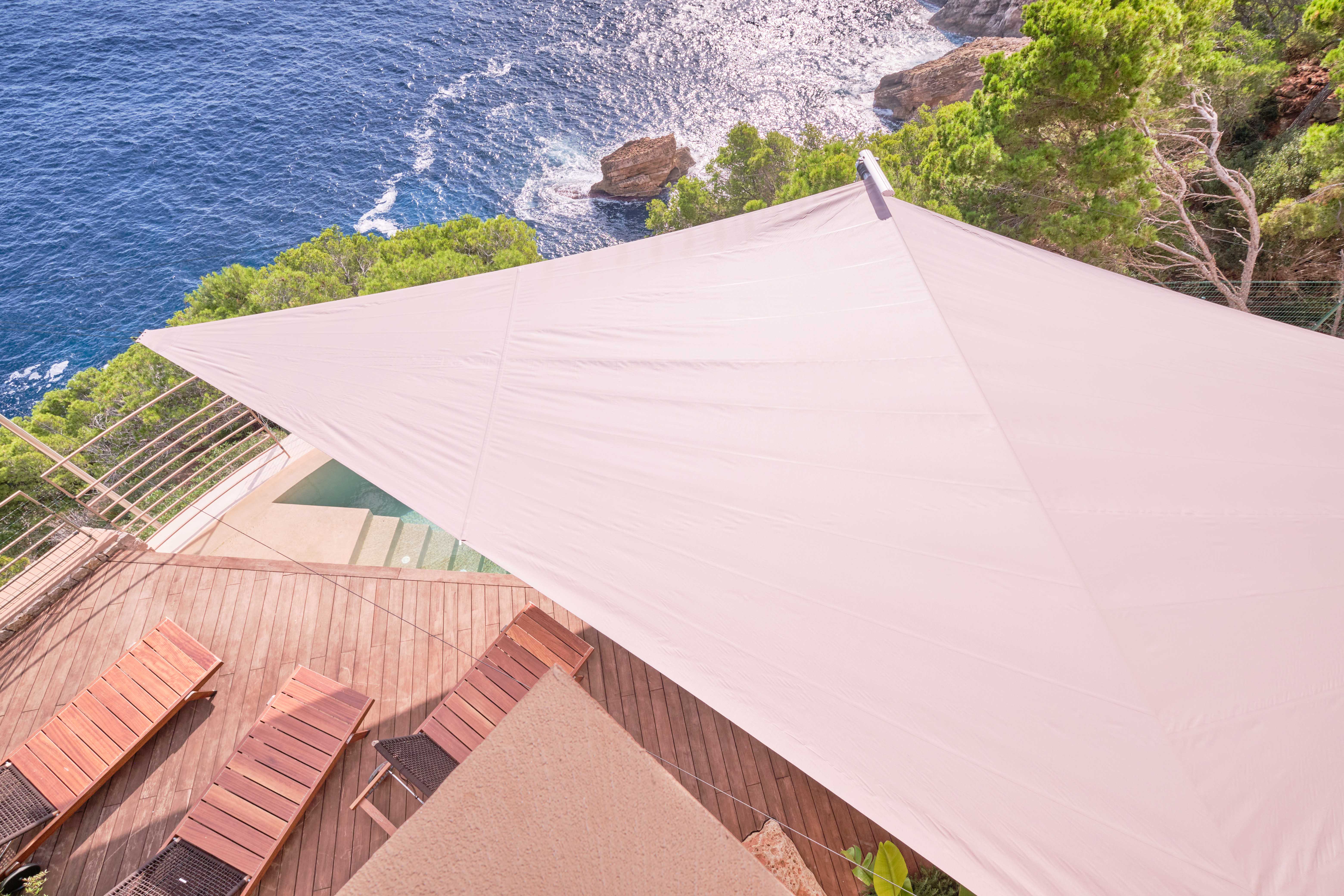 Ein Blick die Steilküste hinunter, man sieht ein Segel von oben und Meter darunter das Meer, das an die Felsen schlägt.