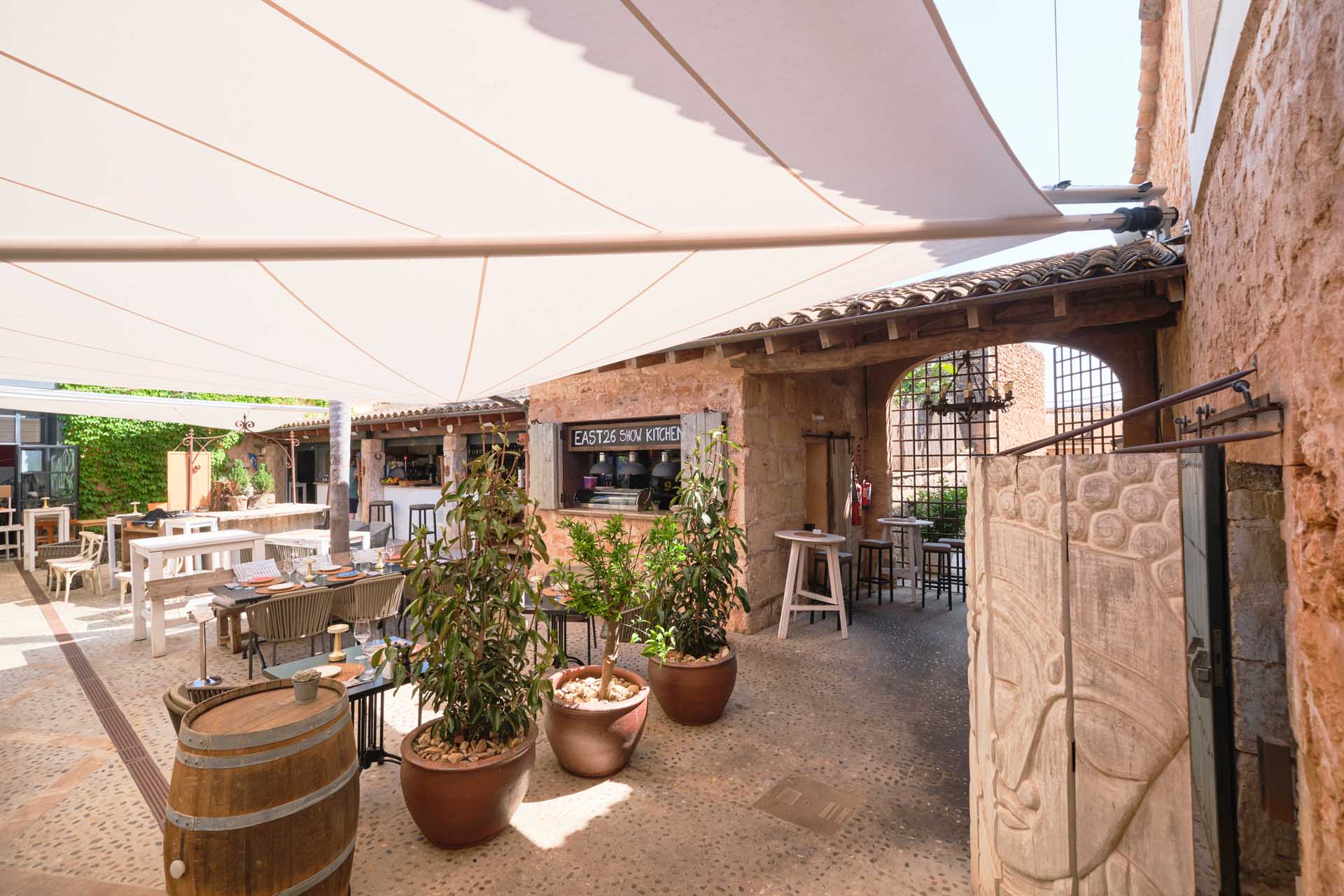 Zwei elektrisch gesteuerte SunSquare-Sonnensegel spenden großflächigen Schatten im mediterranen Innenhof des Restaurants East 26.