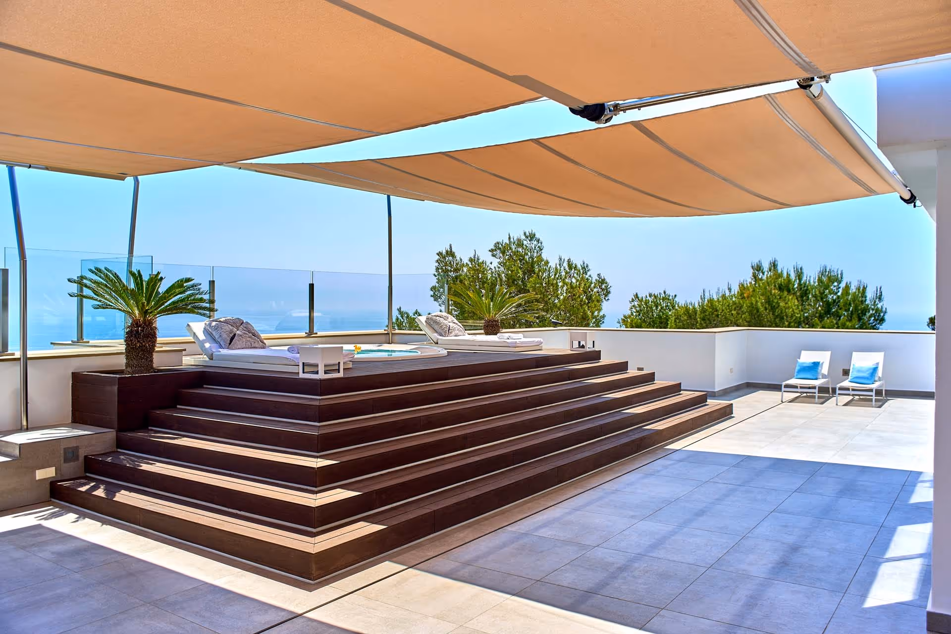 Un piedistallo in legno conduce a una vasca idromassaggio sulla terrazza dell'hotel, protetta dalla luce solare diretta con vele solari SunSquare.