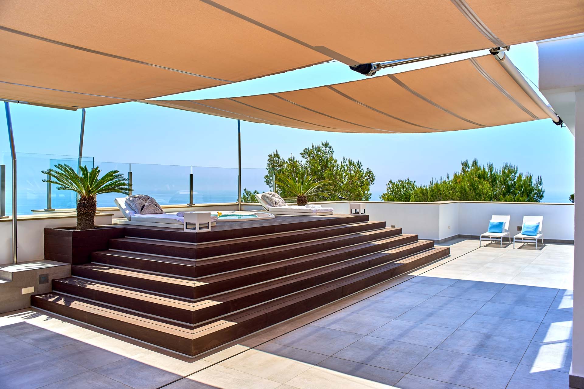 A wooden pedestal leads to a hot tub on a hotel terrace, which is protected from direct sunlight with SunSquare sun sails.