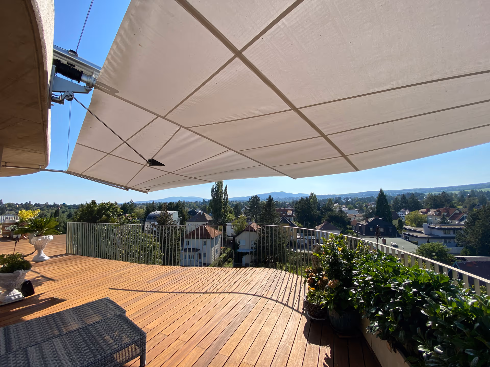 Spacious roof terrace with wooden floors and flower pots with lots of plants with rectangular awning, which prevents the plants from drying out.