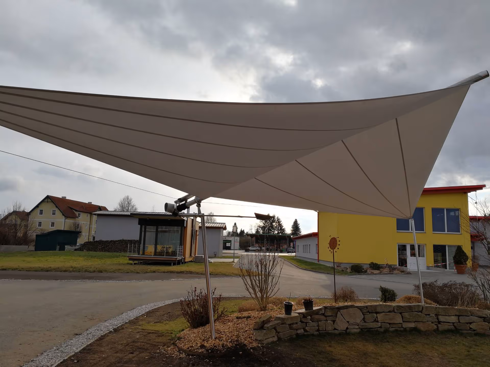 A SunSquare awning is mounted on an open area with the help of two ground supports and a wall mounting point.
