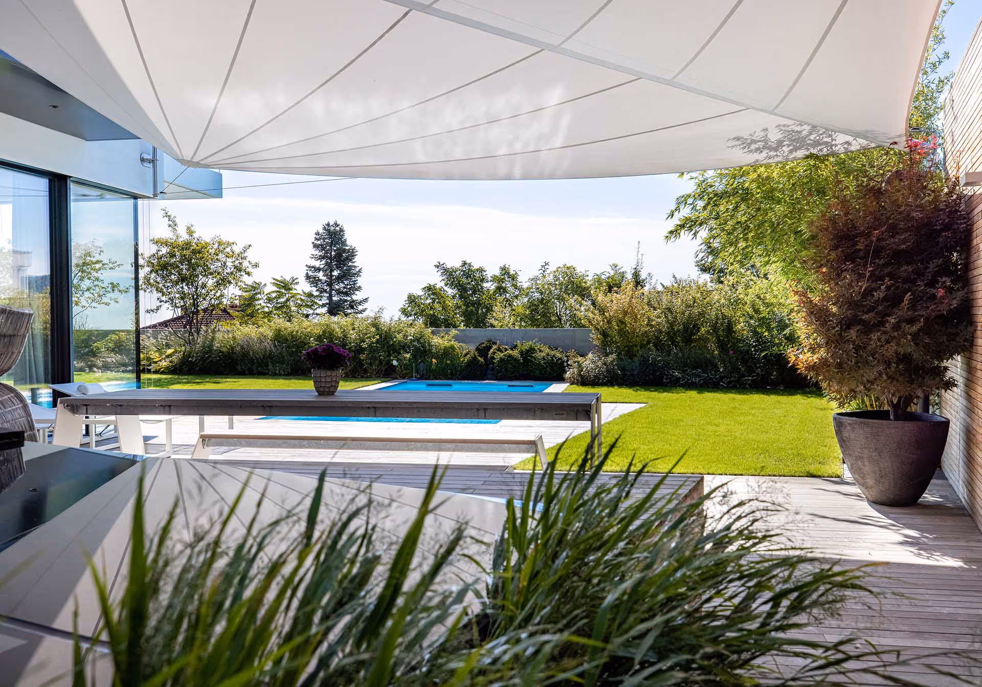 SunSquare Sonnensegel am Poolbereich eines Einfamilienhauses.SunSquare Kompensatoranlage mit 43 m² Segelfläche bietet stilvollen Sonnen- und Regenschutz im Garten.