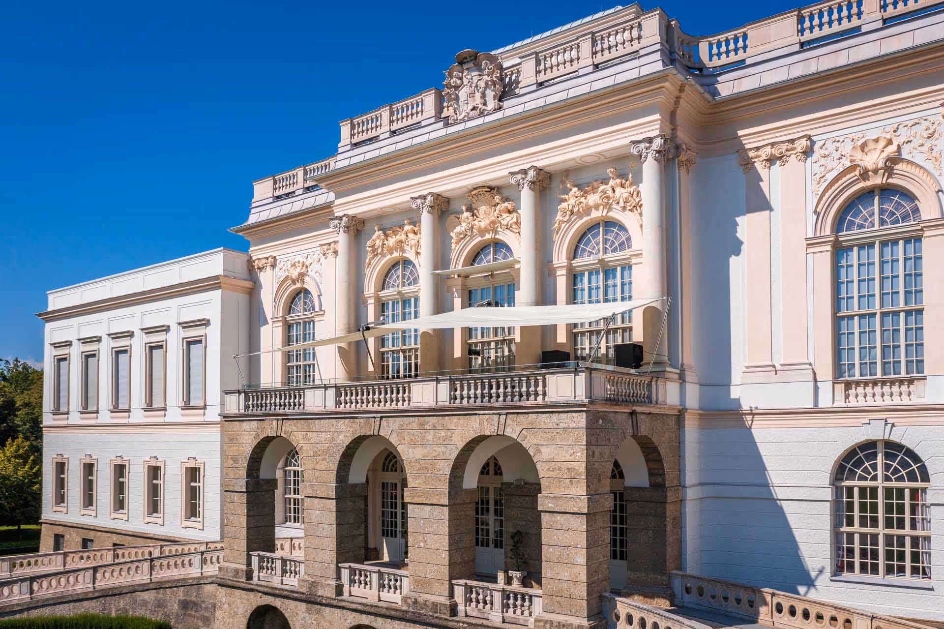 Luftaufnahme des Schloss Kleßheim, in dem das Casino Salzburg verortet ist. Man sieht die Auffahrt und das SunSquare Sonnensgel vor dem Hauptportal.