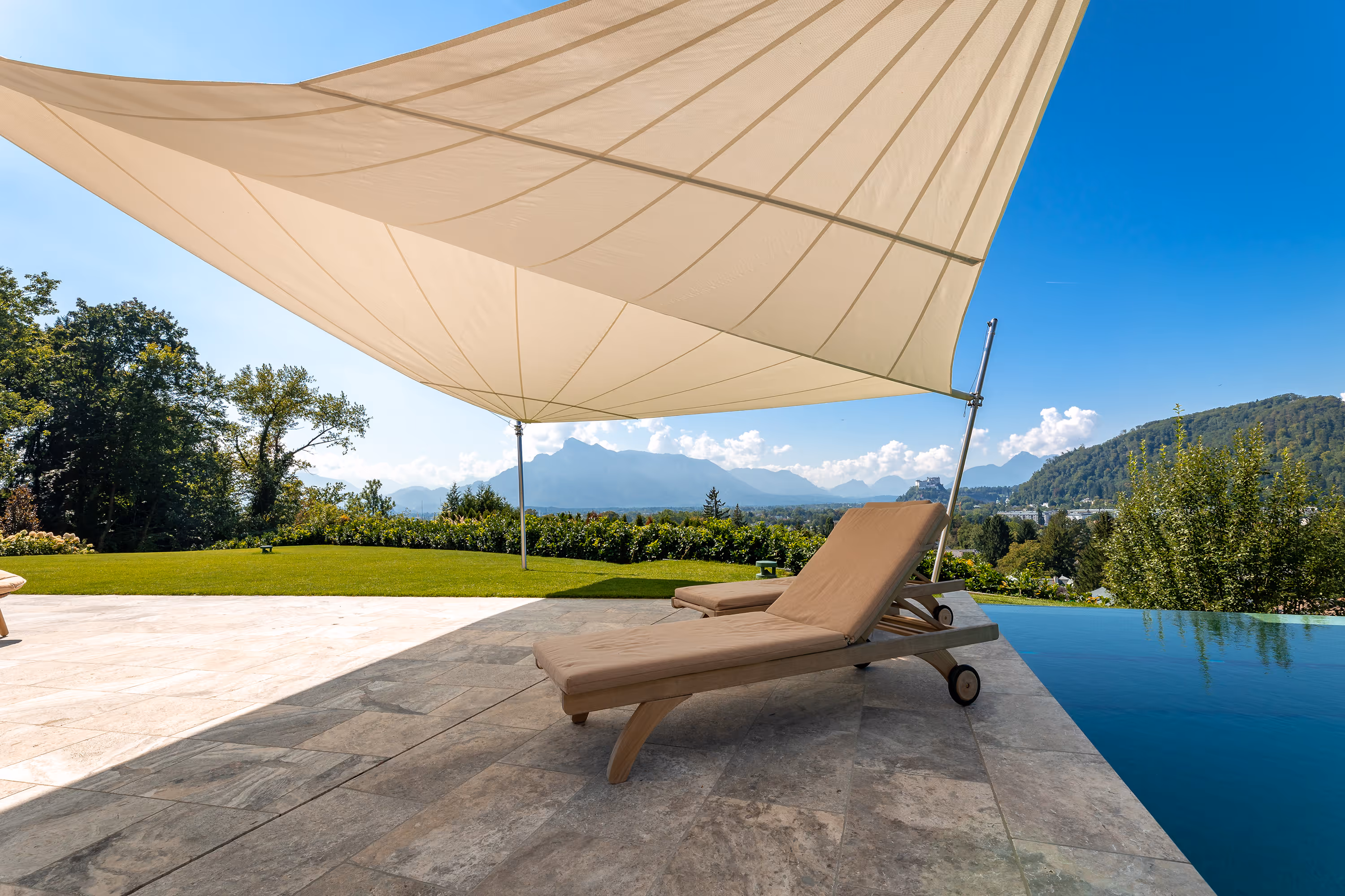 Zwei Loegen am Pool laden zum Verweilen unter dem Sonnensegel-Schatten ein.