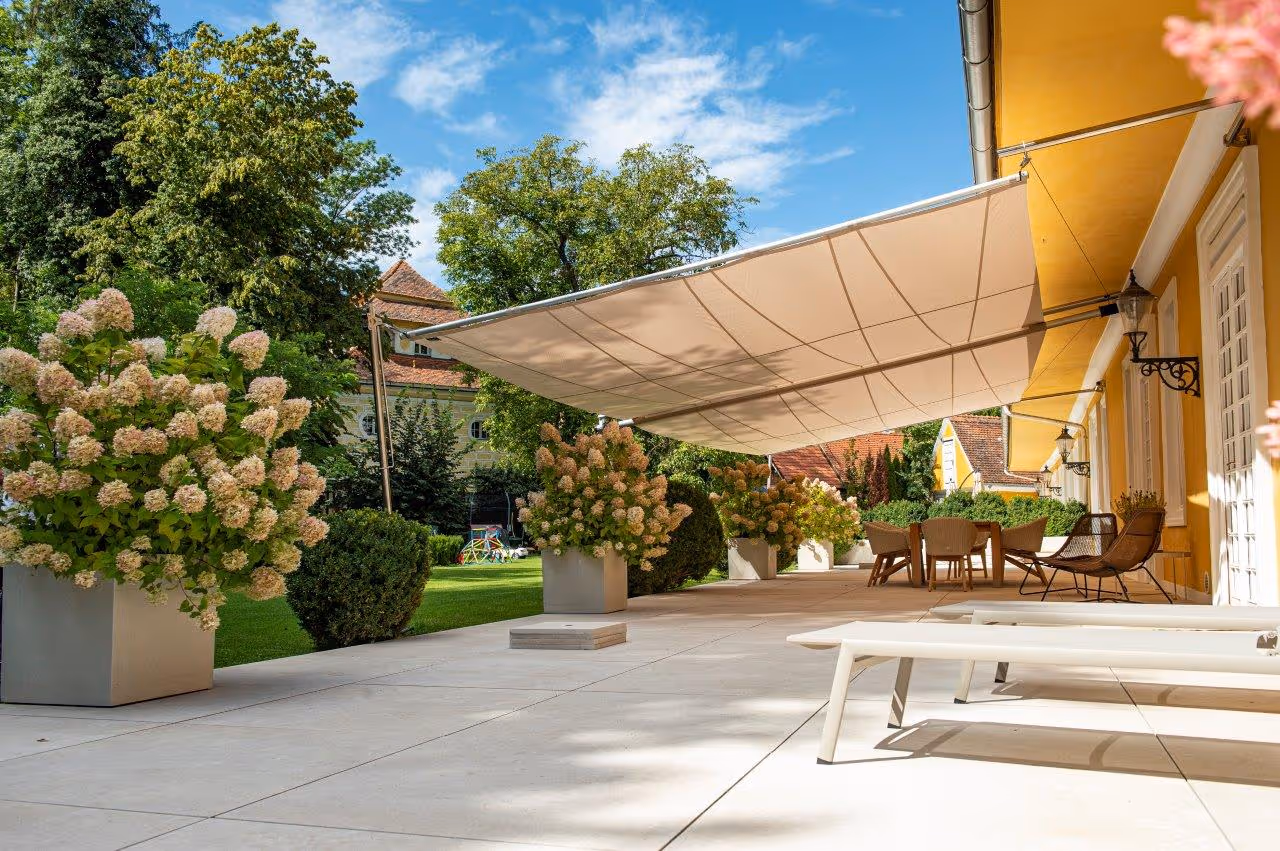 An inviting terrace with lots of plants and a spacious dining area is protected from sun and rain by a rectangular panel on both sides.