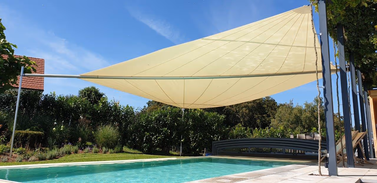 Sun sail over the terrace and pool area with white cloth, outdoor furniture and a well-kept garden in the background — stylish sun and rain protection.