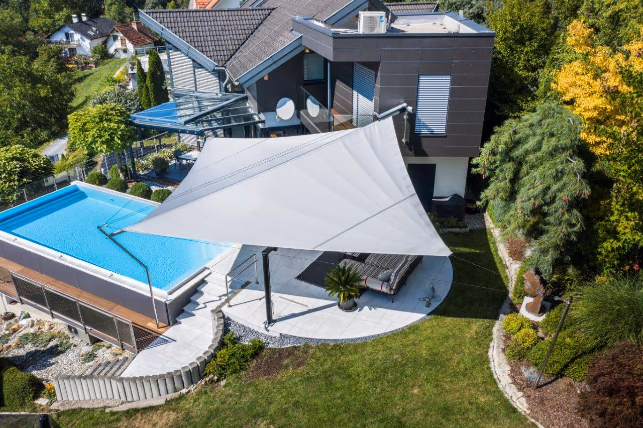 Strahlensegel-Anlage mit eleganter Anbindung an die Stahlkonstruktion eines bestehenden Wintergartens – maßgeschneiderte Lösung für komplexe Terrassensituationen.