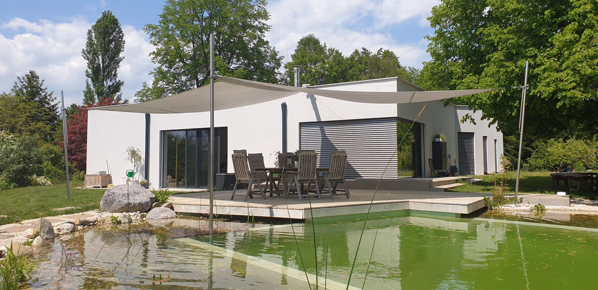 Schwimmteil mit modernem Einfamilienhaus und Badeplattform mit Sonnensegel von SunSquare.