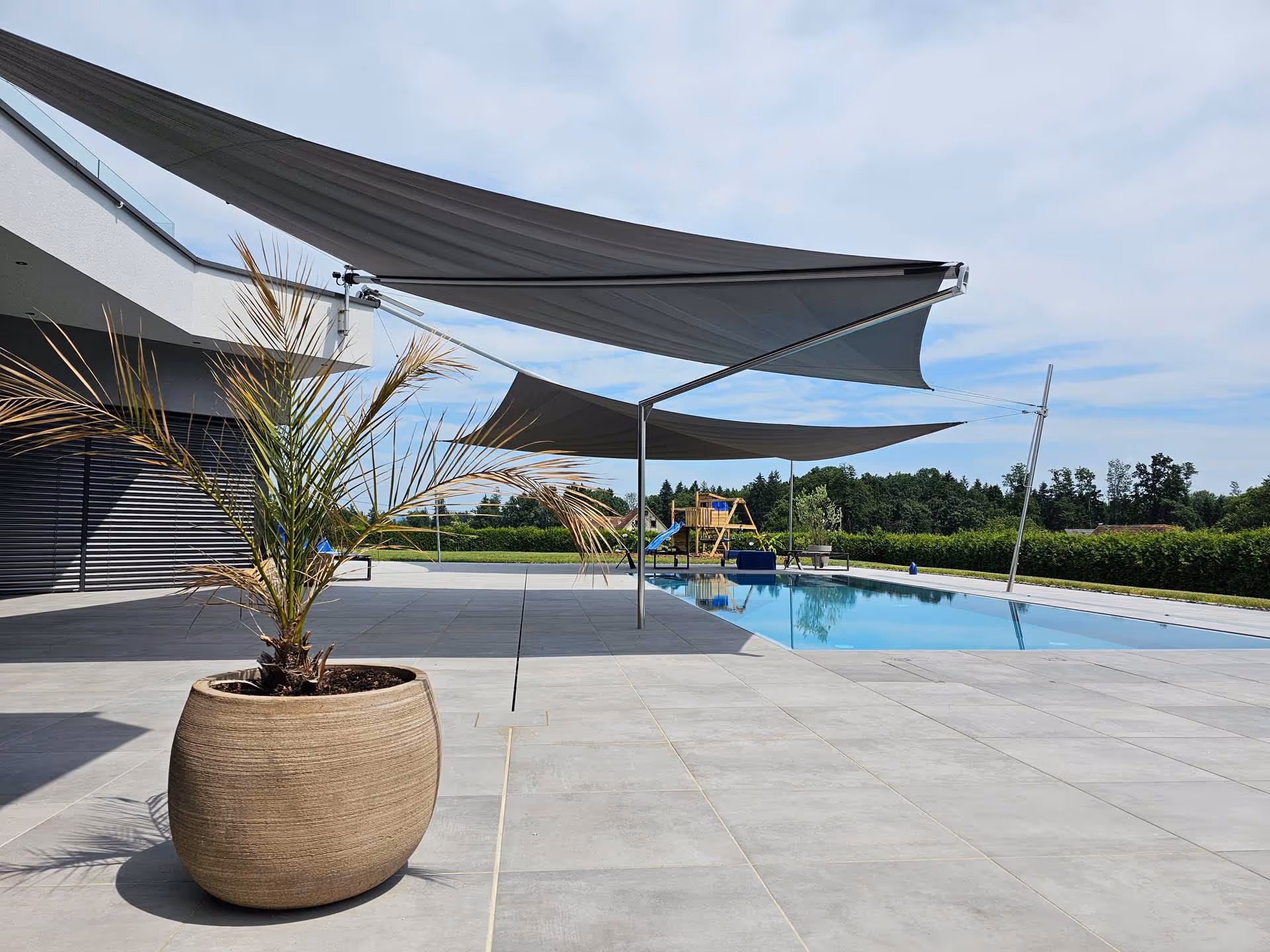 Two custom SunSquare awnings shade a pool and the seating area around the pool. Contemporary look.