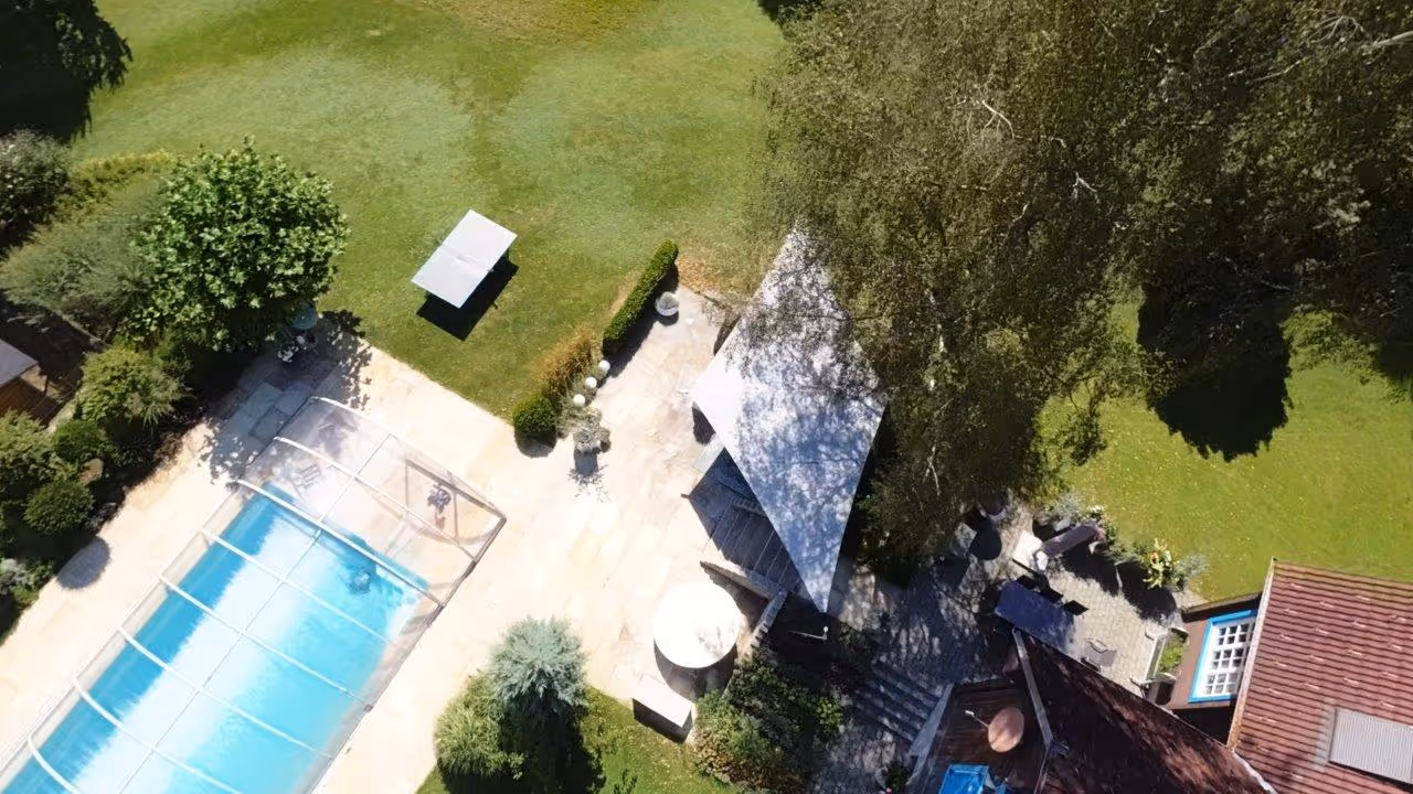 Luftaufnahme des Gartens mit Pool, überdachter Terrasse mit einem SunSquare Cantilever Sonnensegel inmitten einer grünen Gartenlandschaft.