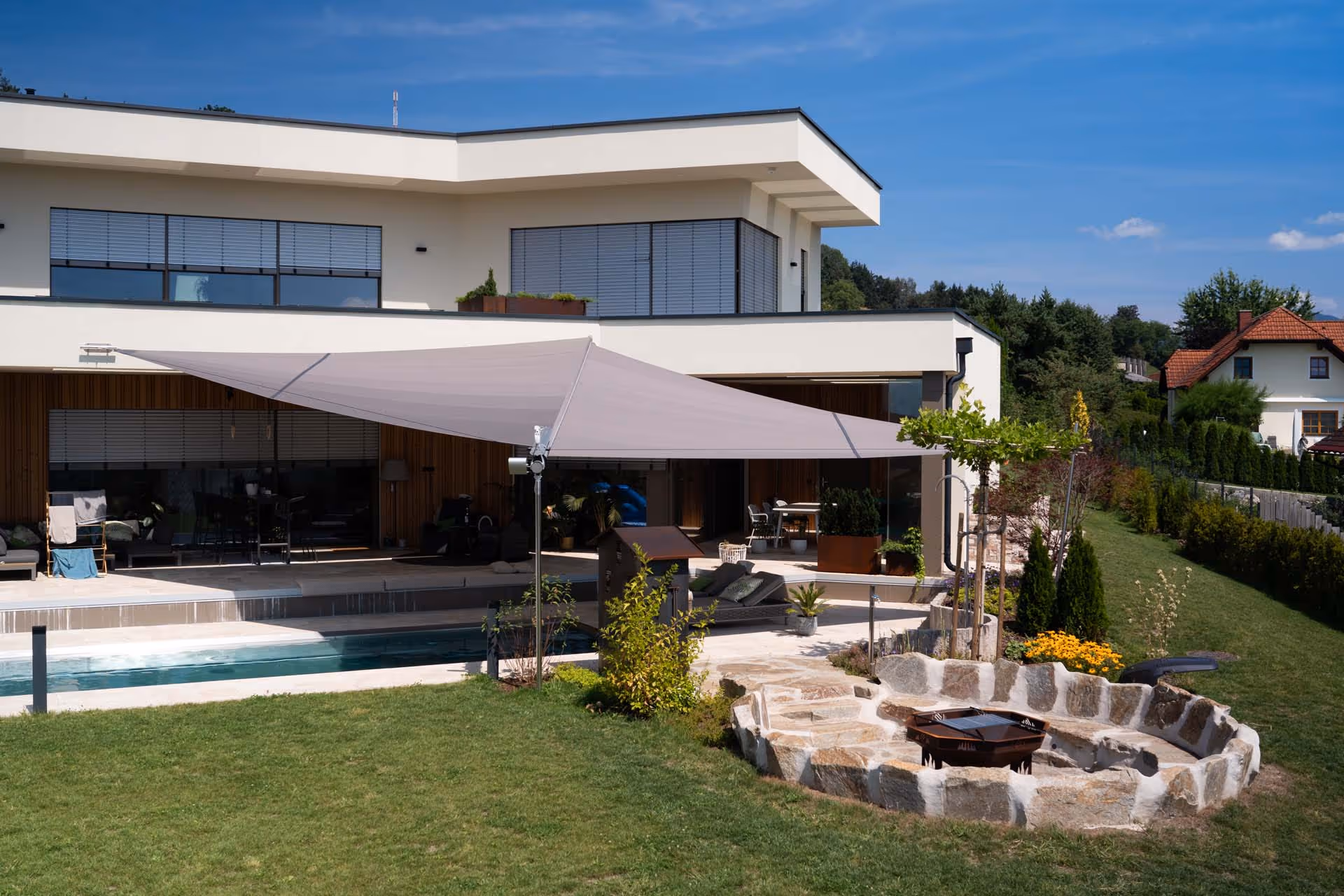 Eine Aufnahme von weiter weg zeigt das Gesamtensemble dieses Projekts - ein architektonisch ansprechendes Haus mit Pool und SunSquare Segel.