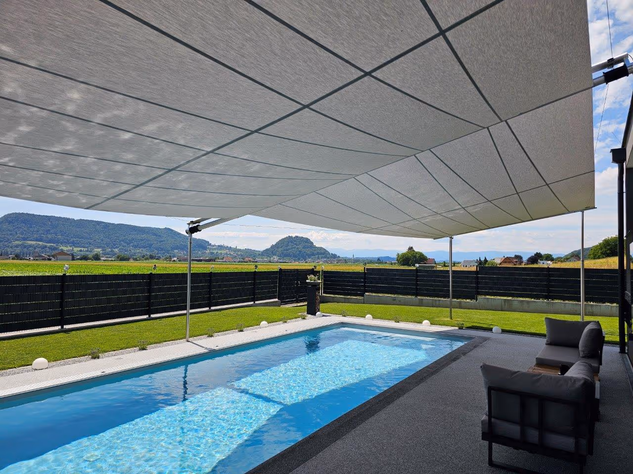 Von unter dem Vordach eröffnet sich der Blick in den Garten – die Schattenwirkung des angrenzenden Segels ist dabei sofort erkennbar.