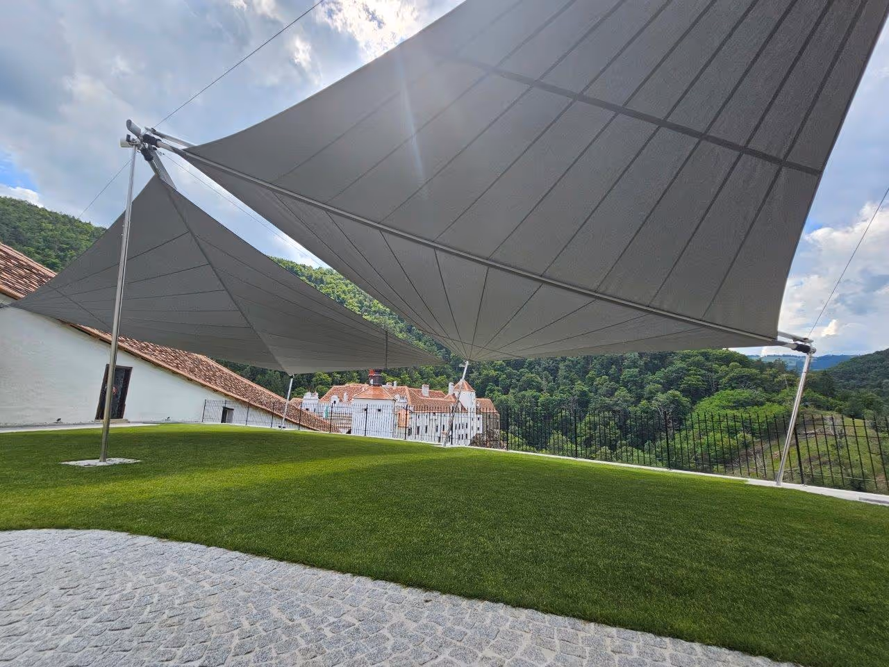 Two large SunSquare sails in the garden of Herberstein Castle, with a view of the historic building and the surrounding hills.