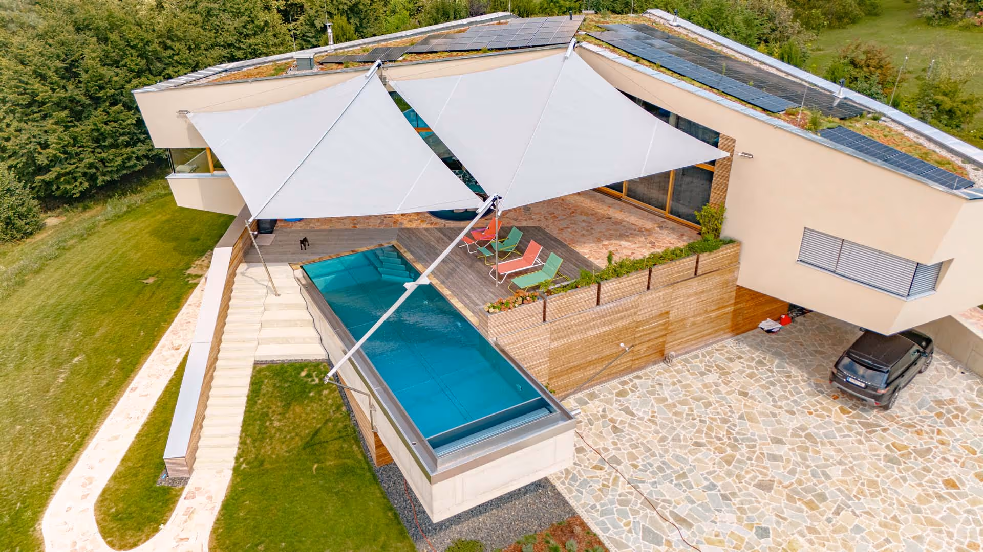 Eine Luftaufnahme. Eine SunSquare Anlage ist geschlossen, zwei sind geöffnet und beschatten den Ess- und Sitzbereich neben dem Pool. 