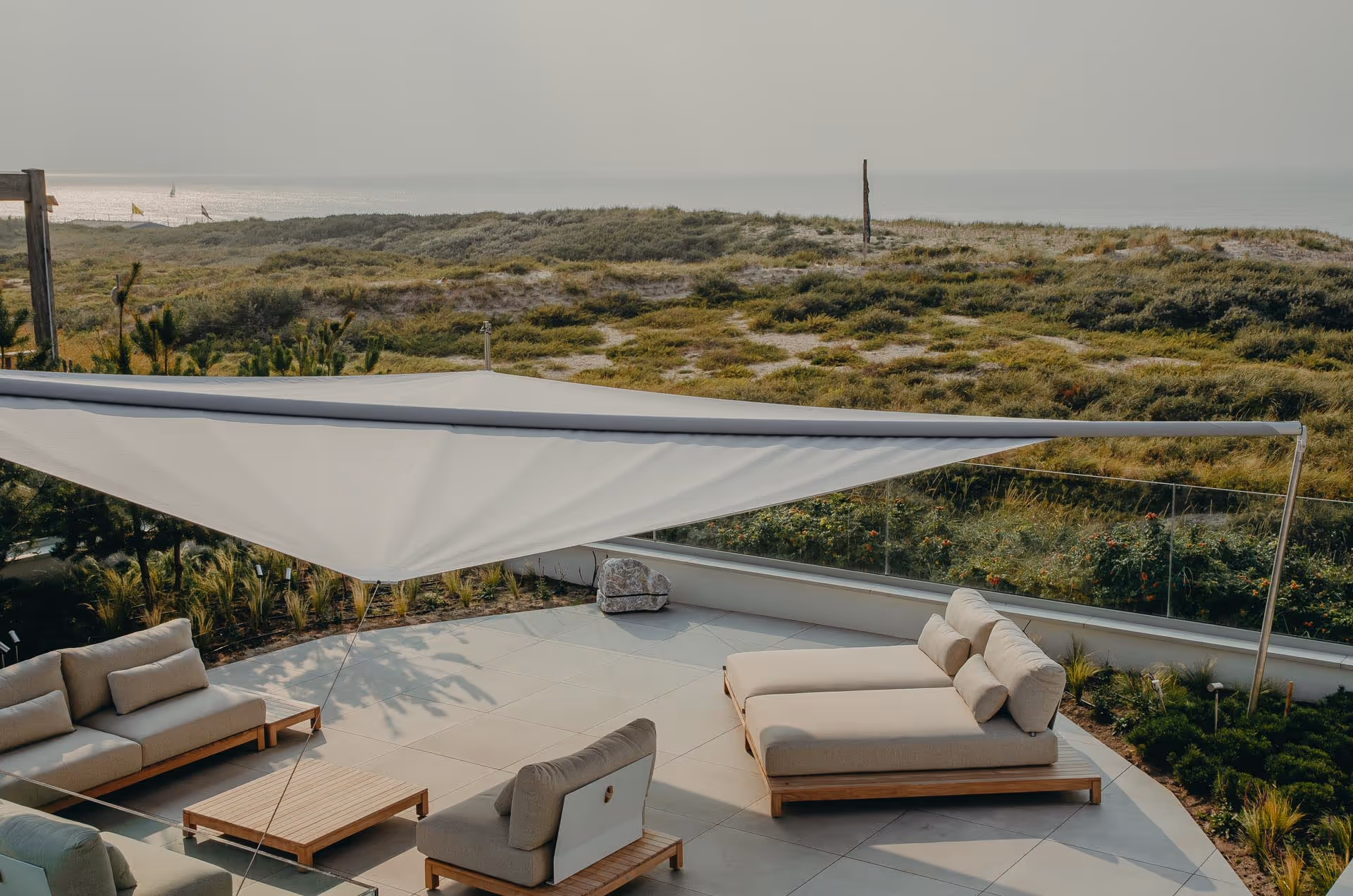 Elegant roof terrace with a 64 m² Sattler 314-082 awning, stylish outdoor furniture and lots of glass, with a view of a green landscape.