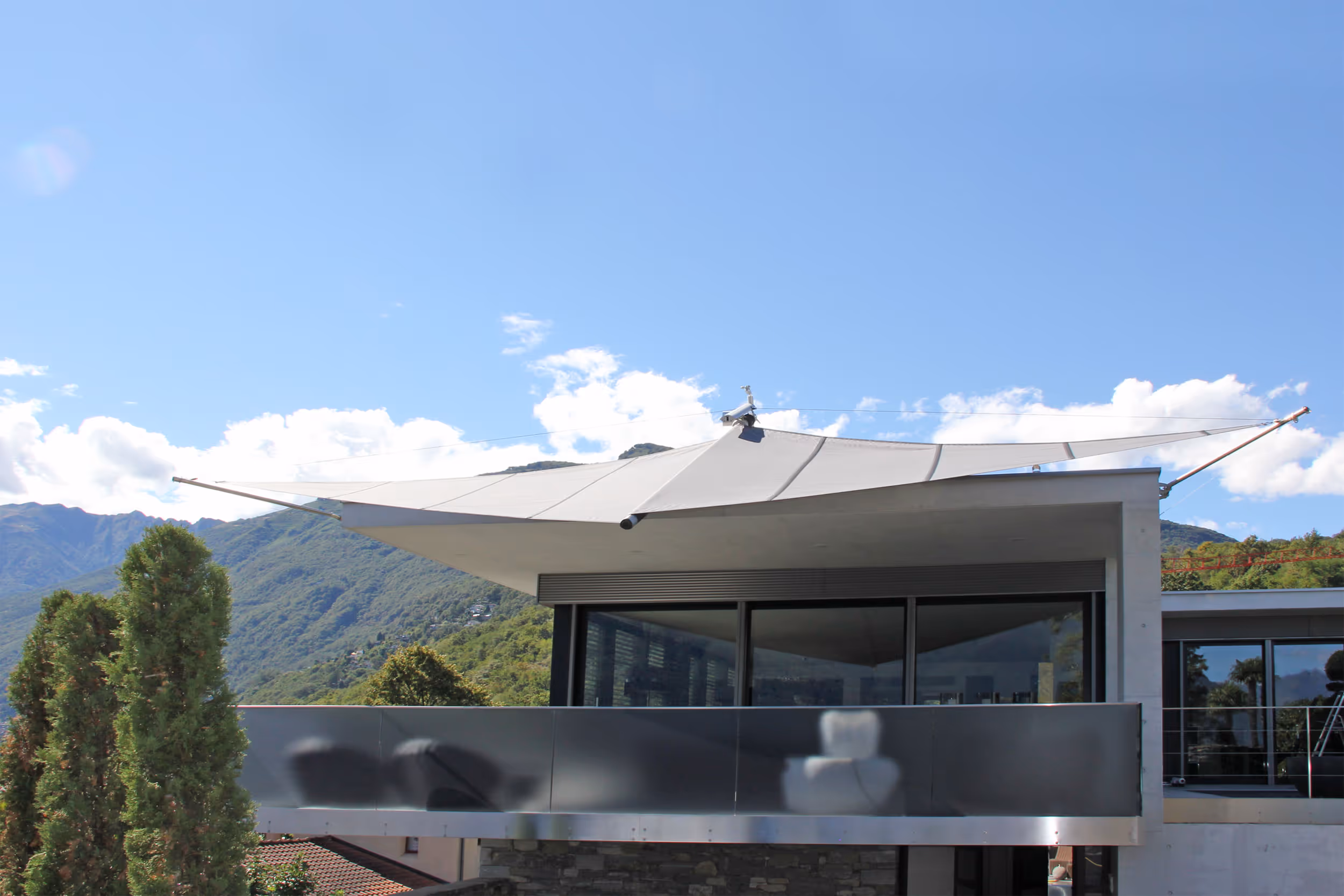 Schräg auskragende SunSquare-Tuchwelle vom Dach – markantes Design mit effektiver Beschattung für Terrasse und Glasfassade.