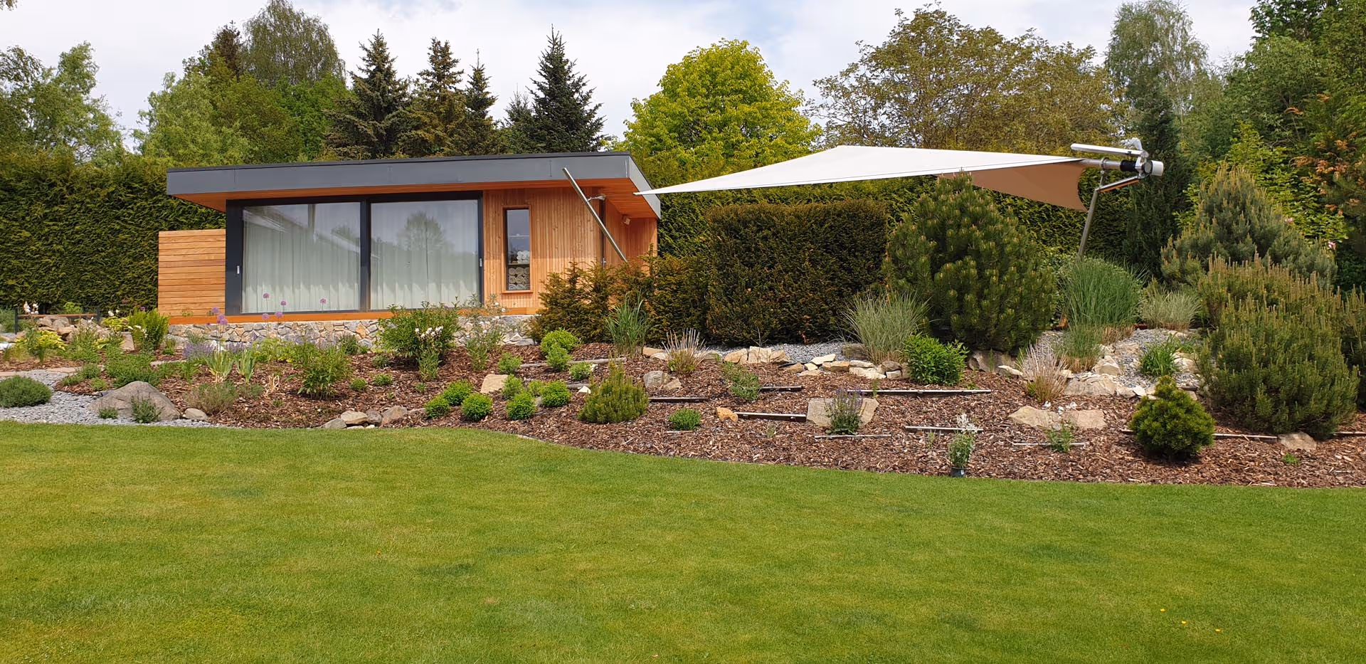 Eine Aufnahme von der Seite von dem Pool auf einer Anhöhe und dem angrenzenden Holzhaus.