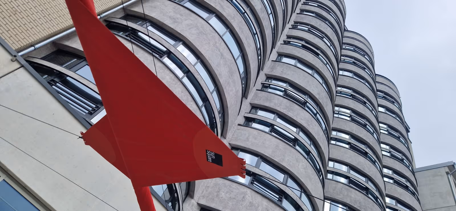 Atmosphärische Nachtaufnahme der Hotelterrasse mit rot akzentuierten SunSquare-Segeln und warmem LED-Licht – Design und Funktion in perfekter Harmonie.