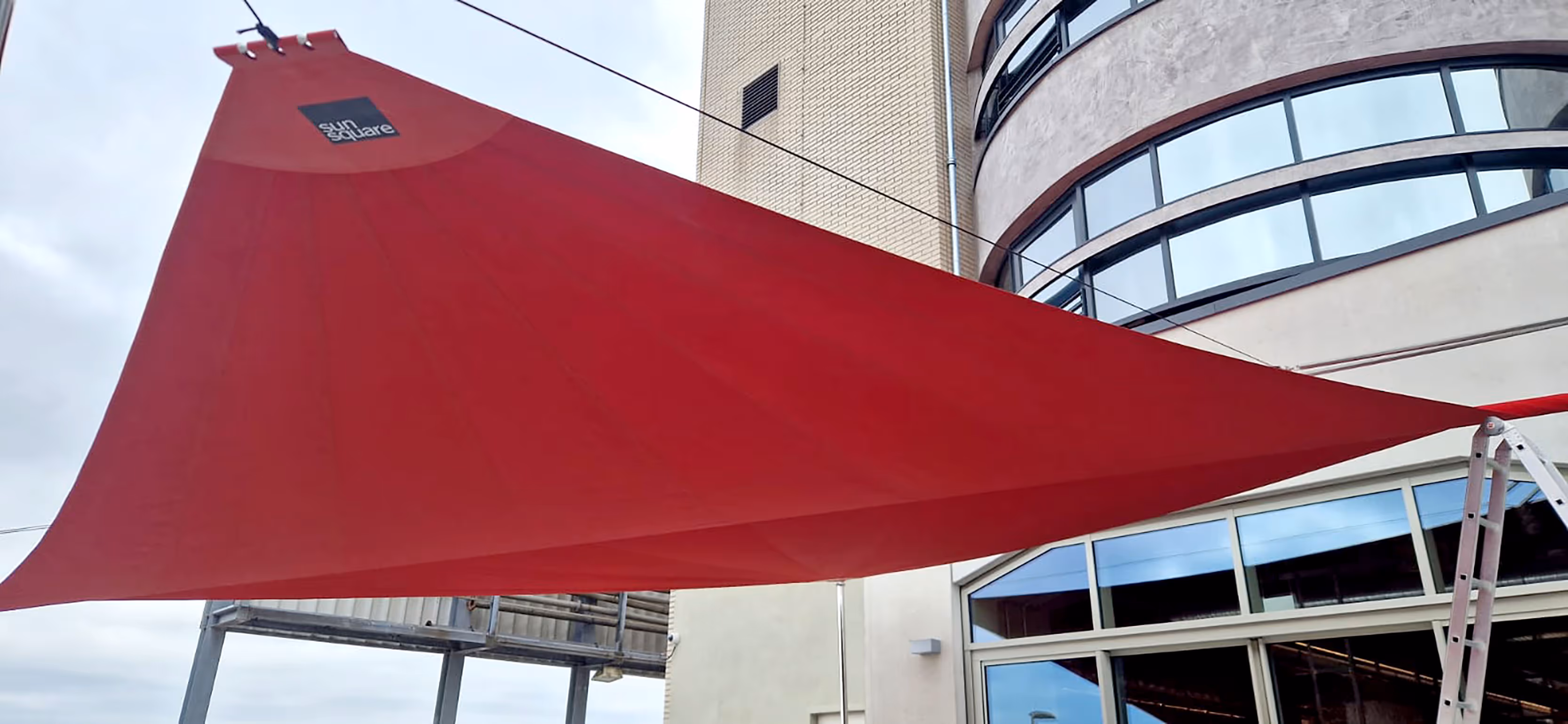 SunSquare-Segel in kräftigem Rotton (DICKSON Infinity Rouge) über der Hotelterrasse – stilvoller Sonnen- und Regenschutz für Gäste.