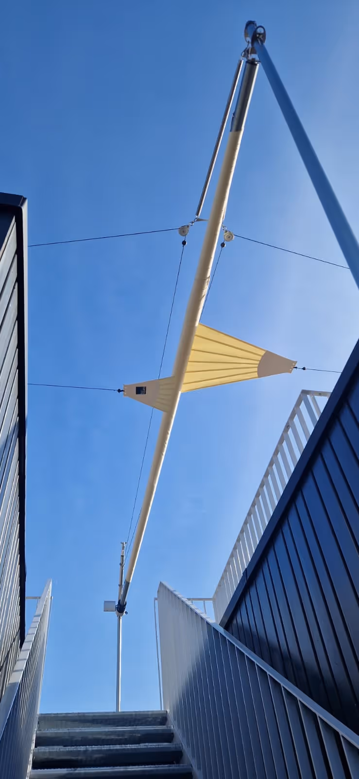 Geschlossenes SunSquare Sonnensegel von unten fotografiert. Man sieht den Stiegenaufgang auf die Dachterrasse.