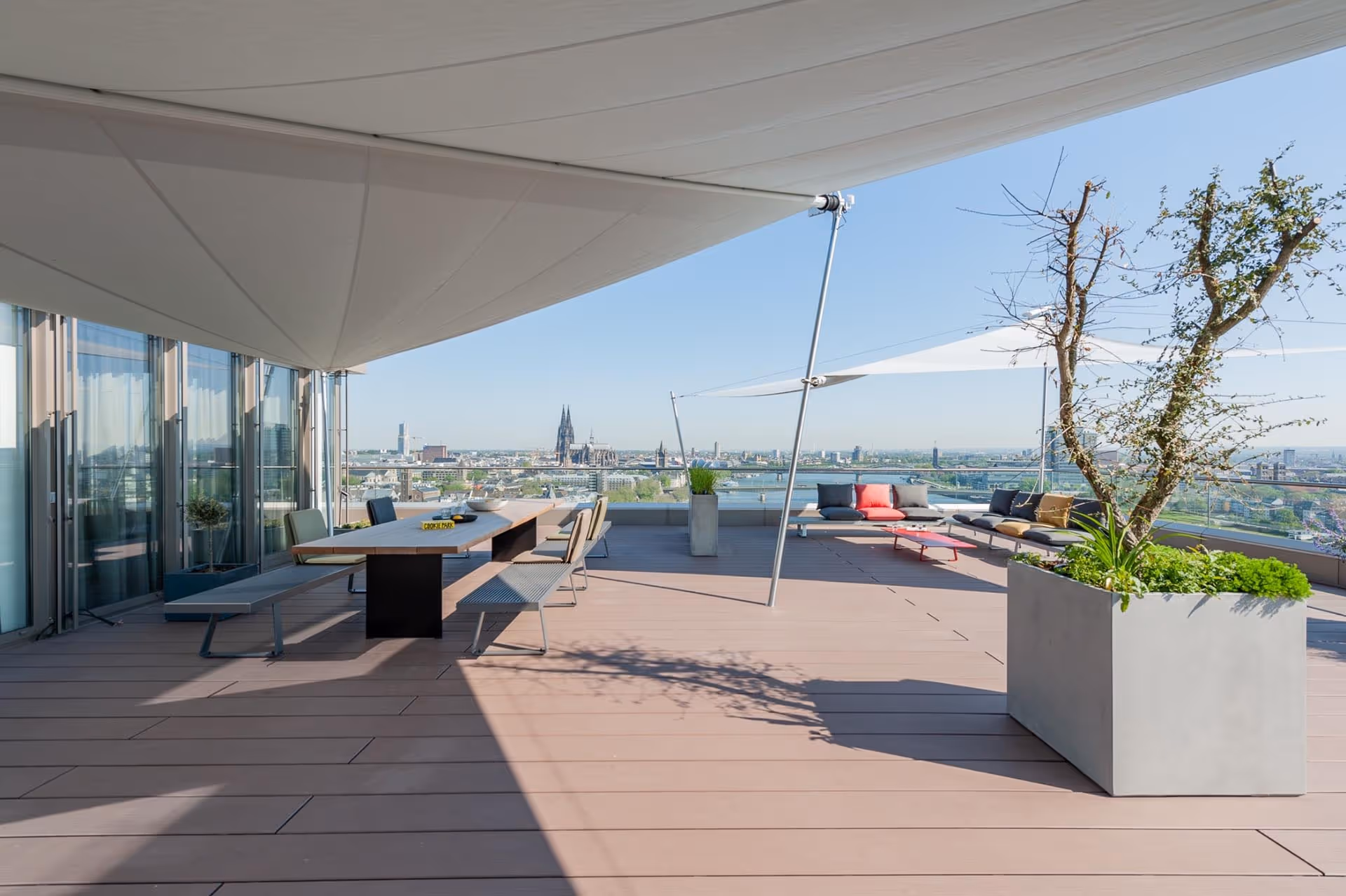 Strahlender Sonnenschein und Schatten durch die SunSquare Sonnensegel mit Weitblick auf den Kölner Dom.