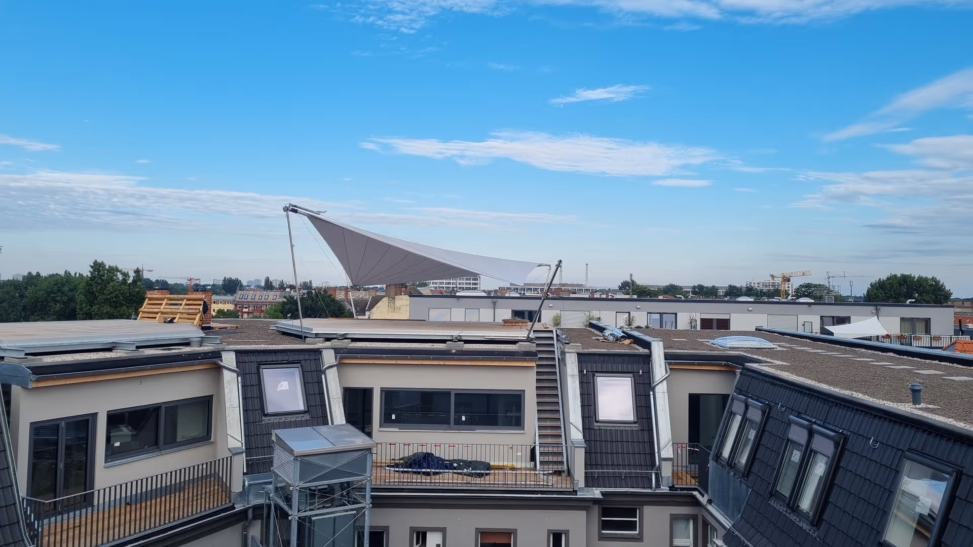 Ein Blick von weiter weg: Dachterrasse mit großflächigem SunSquare Sonnensegel in Hellgrau – montiert auf Stahlrahmen mit elektrischen Höhenverstellern über Berlin