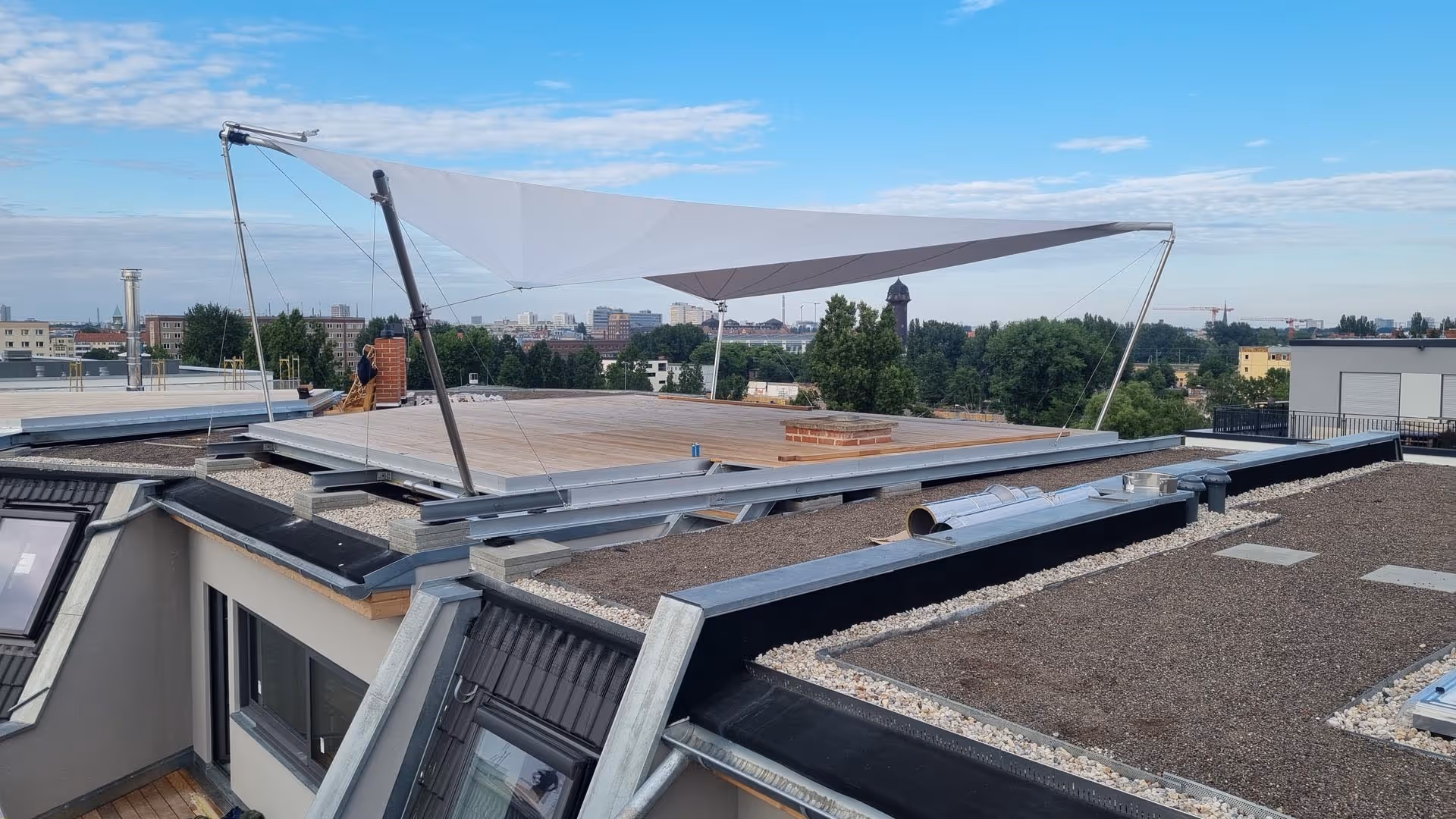 Baustelle: Dachterrasse mit großflächigem SunSquare Sonnensegel in Hellgrau – montiert auf Stahlrahmen mit elektrischen Höhenverstellern über Berlin