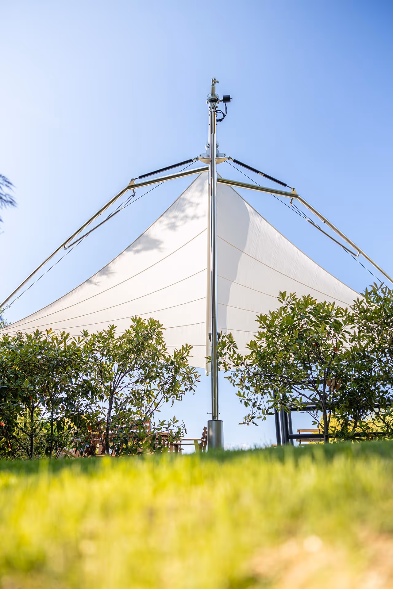 Fold & Roll Segelschirm spendet flexiblen Schatten in einem weitläufigen Garten mit Zypressen und italienischer Architektur.
